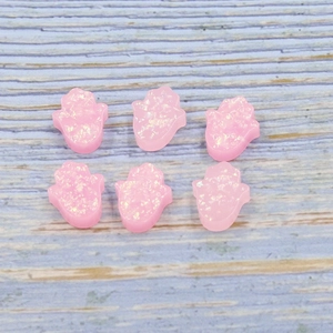 Set of six pink resin Hamsa opal hand beads with subtle glitter on a wood background