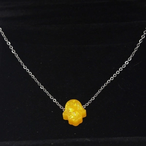 Macro view of a yellow Hamsa hand opal pendant on a silver chain over black velvet