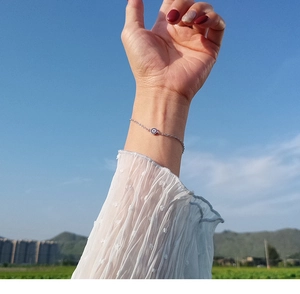 Close-up of a silver Evil Eye bracelet worn on a wrist against a clear blue sky