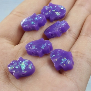 Macro shot of purple Hamsa beads with holographic glitter held in hand for DIY jewelry