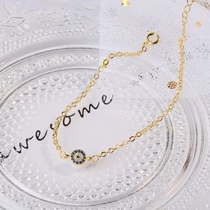 Golden chain bracelet with blue evil eye pendant on a decorative textured glass tray
