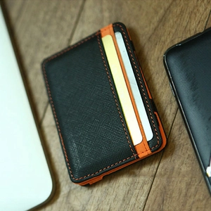 Minimalist magic wallet in black textured leather with vibrant orange stitching on wood