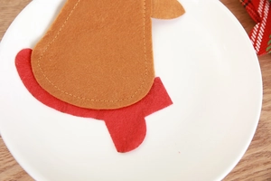 Detail of felt Santa cutlery holder with red and brown stitching on white plate