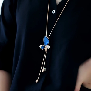 Detailed view of butterfly pendant with blue crystals on gold chain necklace worn by model