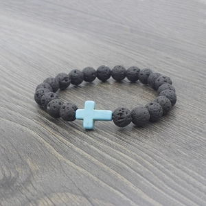 Macro shot of black lava rock beads and a light blue cross charm on a wooden surface