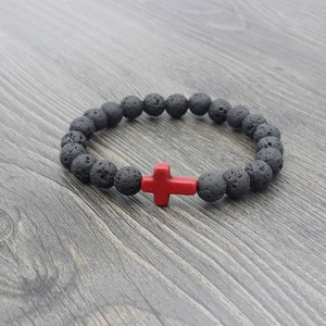 Close-up of black lava stone beads bracelet with a vibrant red cross pendant on wood
