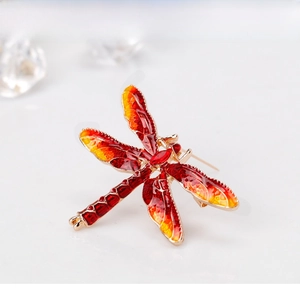 Macro view of a gold-framed dragonfly brooch with red and yellow enamel detailing