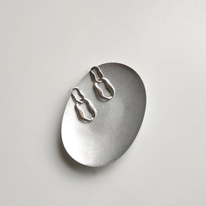 Detailed view of silver geometric chain earrings on an oval matte metal tray display