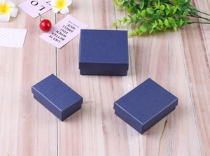 Three deep blue linen textured jewelry boxes for rings and necklaces on wood surface