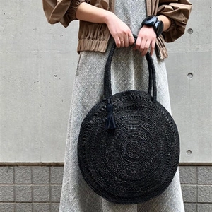 Detail of a black woven mesh handbag featuring a wooden handle and matching tassel fringe
