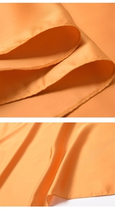Close-up of orange silk scarf showing precision stitching and smooth satin texture