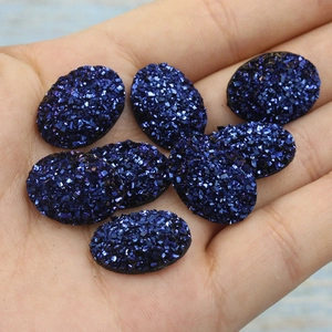 Macro shot of dark blue oval resin cabochons with sparkling druzy texture on a hand
