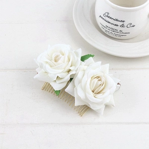 Detail of two white velvet faux roses with green leaves on a gold metal hair comb