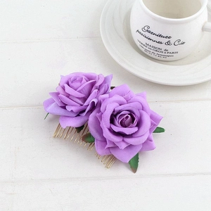 Detail of dual purple fabric roses and green leaves on a gold bridal hair comb