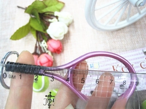 Close-up of a purple metal tennis racket keychain with black grip, measuring about 9cm