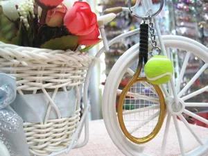 Close-up of golden tennis racket and green felt ball keychain with metal chain link