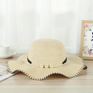 Detail of straw sun hat with decorative black band, pearls, and wavy scalloped edge trim