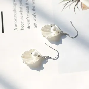 Elegante Muschel-Ohrringe mit weißen Perlen und Silberhaken auf einem Magazinhintergrund