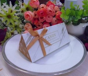 Detail of marble pattern wedding candy box with golden ribbon on a white plate