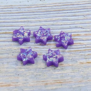 Five purple synthetic opal star-shaped jewelry charms on a light wood grain background