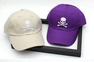 Detail of embroidered skull logos on beige and purple cotton baseball caps in flat lay