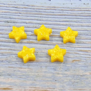 Close-up of five yellow resin star-shaped beads with 1.5mm holes on a wood surface