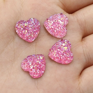 Roze hartvormige harskristallen met glittertextuur getoond op een hand voor schaal