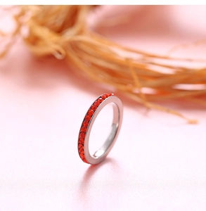 Detailed close-up of a silver band ring with red round-cut crystals on a pink surface