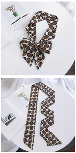 Detail of paisley pattern silk scarf tied in a bow and laid flat on a white table
