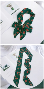 Detail of dark green silk scarf with red geometric pattern tied as a bow on a white desk