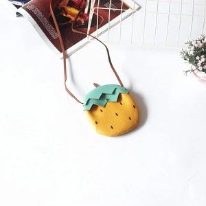 Close-up of yellow strawberry-shaped kids' crossbody bag with lychee texture and green leaves