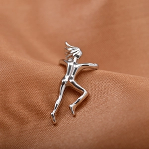 Close-up of a silver gymnast figure ear cuff on soft peach textured fabric