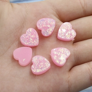 Detail of pink heart-shaped resin cabochons with iridescent opal fire effect on palm