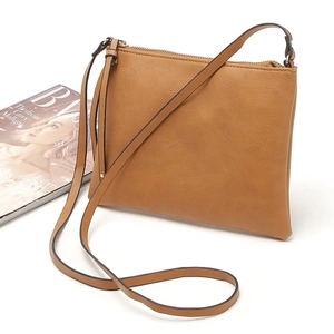 Close-up of brown faux leather envelope bag with a thin strap next to a fashion magazine