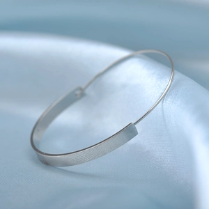Macro shot of minimalist silver metal curved bracelet on soft blue silk fabric