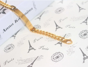 Close-up of golden stainless steel ID Cuban chain bracelet with polished metal nameplate