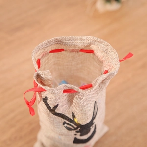 Detail of Christmas reindeer burlap gift bag with red drawstring on a wooden surface