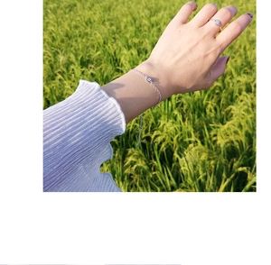 Close-up of silver evil eye bracelet and ring set worn by model in a natural setting