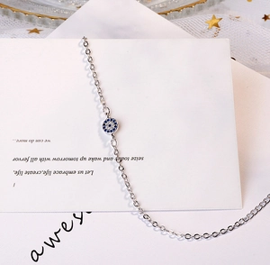 Macro shot of silver evil eye bracelet with blue crystal on a white display card