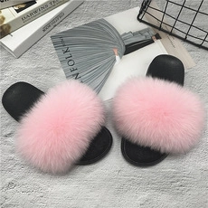 Close-up of plush pink mink fur slides with thick black soles on stylish magazine background