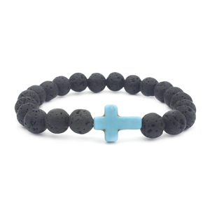 Macro detail of natural black lava rock beads and a light blue cross charm on the bracelet