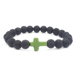 Macro shot of black volcanic lava rock beads with a single green cross charm on a bracelet