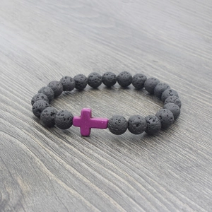 Macro detail of black lava stone beads and purple cross charm on dark wood background