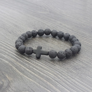 Detailed close-up of natural black lava rock beads and matte cross charm on elastic bracelet