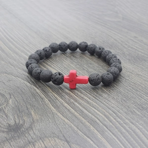 Macro shot of black volcanic lava beads and a red cross on a wood surface
