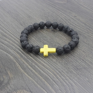 Detail of black lava rock beaded bracelet featuring a yellow cross on dark wood