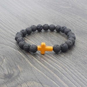 Detail of black lava stone bead bracelet with a vibrant orange cross on gray wood