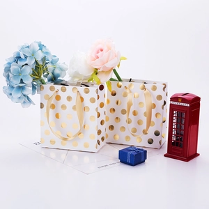 Detail of premium white paper gift bags featuring gold foil polka dots and ribbon handles