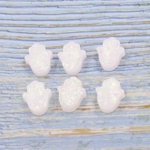White synthetic opal Hamsa hand beads with iridescent luster on striped wood background