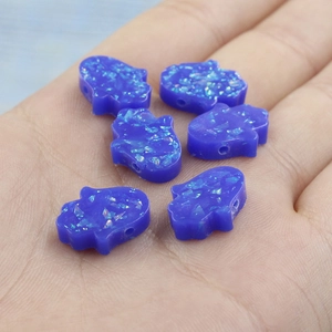 Macro shot of 6 dark blue opal Hamsa beads with glitter detail on a palm